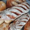 Close-up of rustic flour-dusted baguettes with diagonal slashes in a pile of artisanal bread
