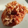 Round pastry or bun topped with thin, curled dried fish flakes (bonito) on a light plate.