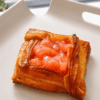 Danish pastry with a glossy pink peach filling on a white plate, close-up view.