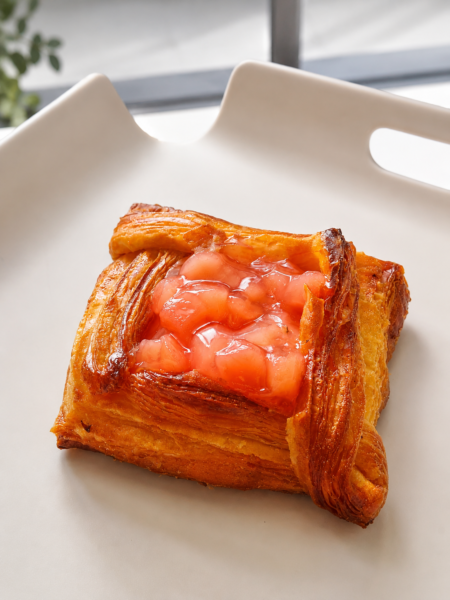 Danish pastry with a glossy pink peach filling on a white plate, close-up view.